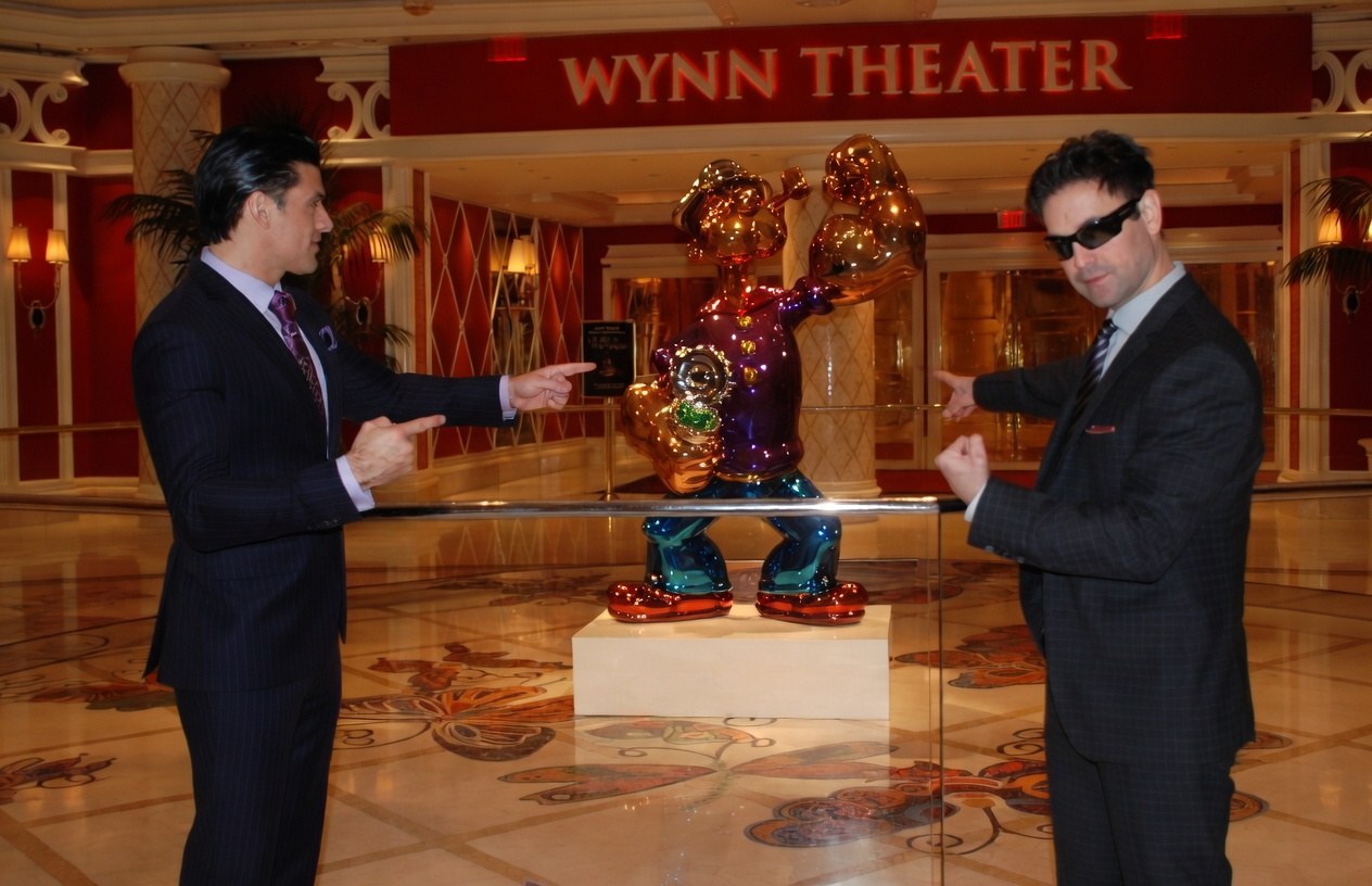 Bobby Catalano and Jason Pascoe in suits pointing at the Popeye statue outside the Wynn Theater in Las Vegas