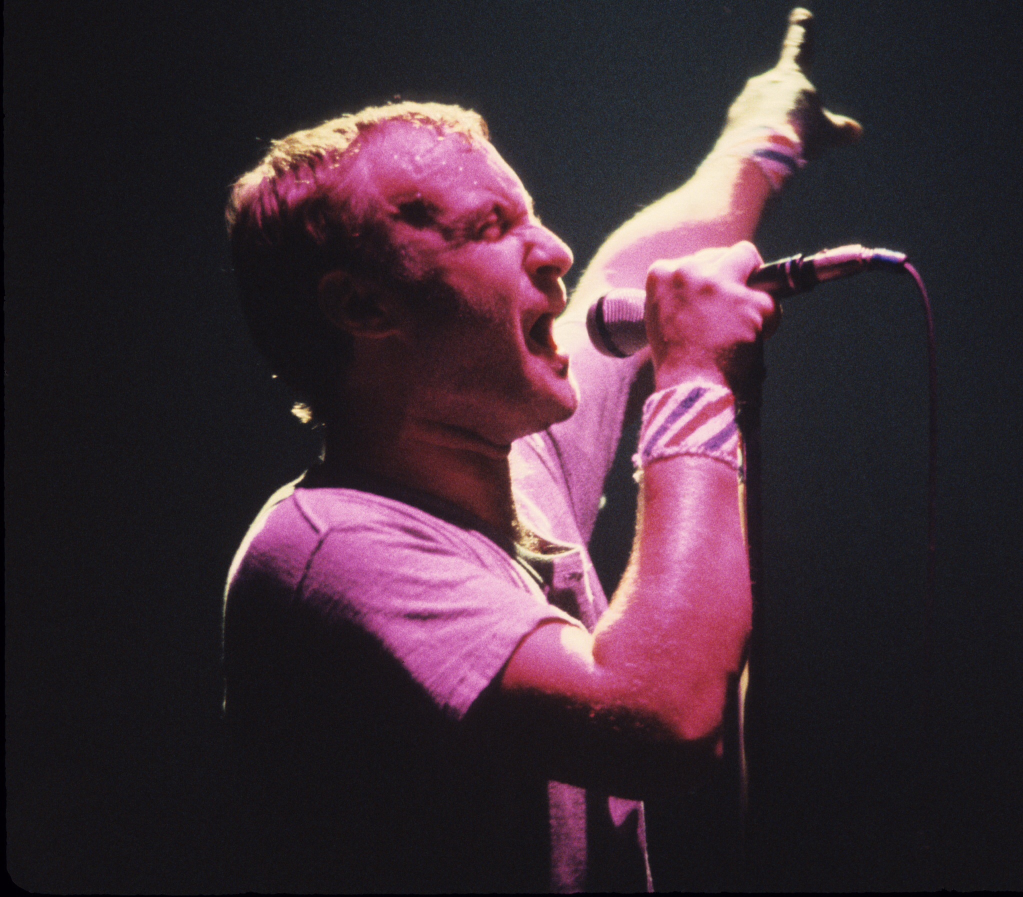 Phil Collins singing into a microphone with one arm raised on stage in 1981